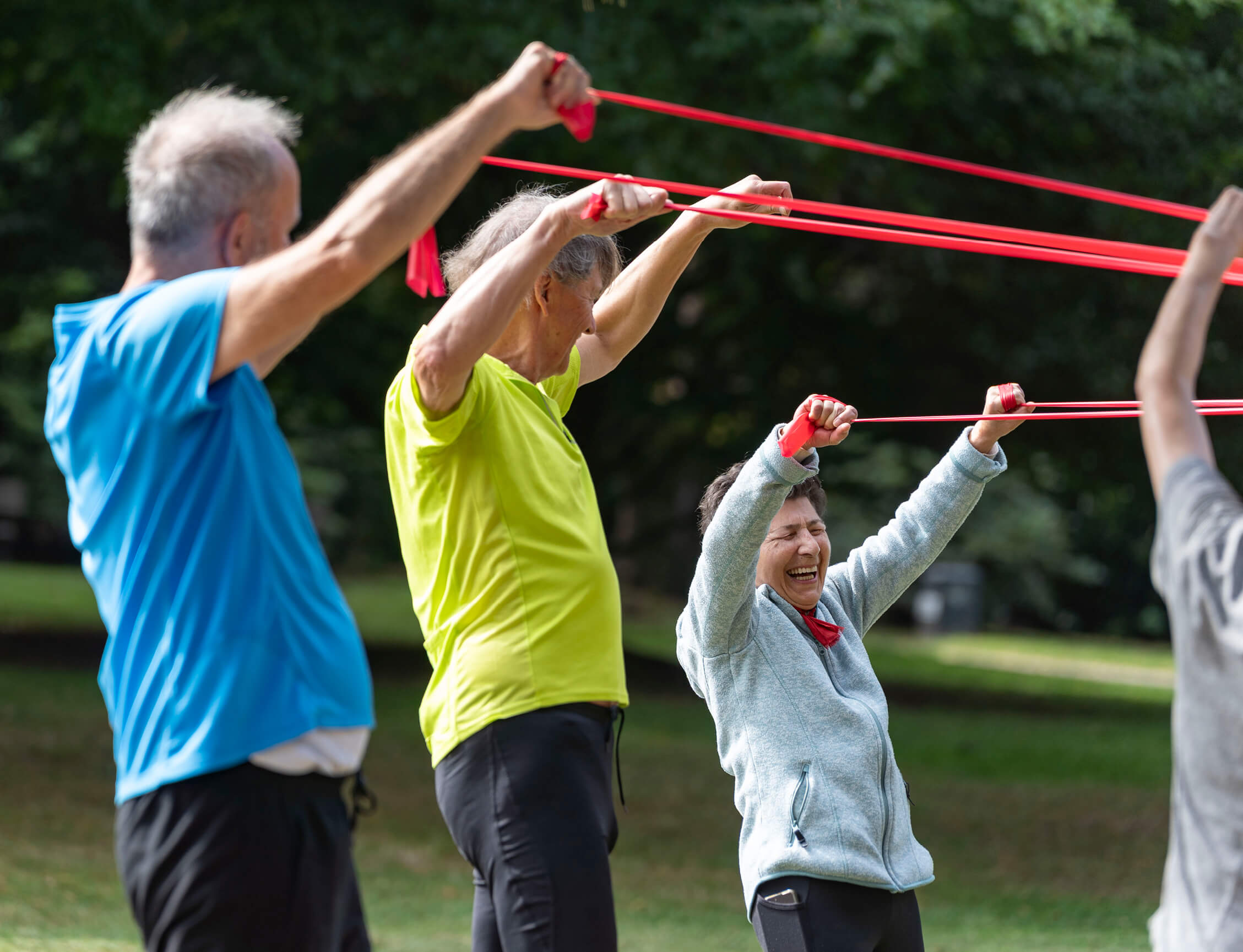 Zwei ältere Männer und eine ältere Frau trainieren mit Therabändern im Park bei Sonnenschein
