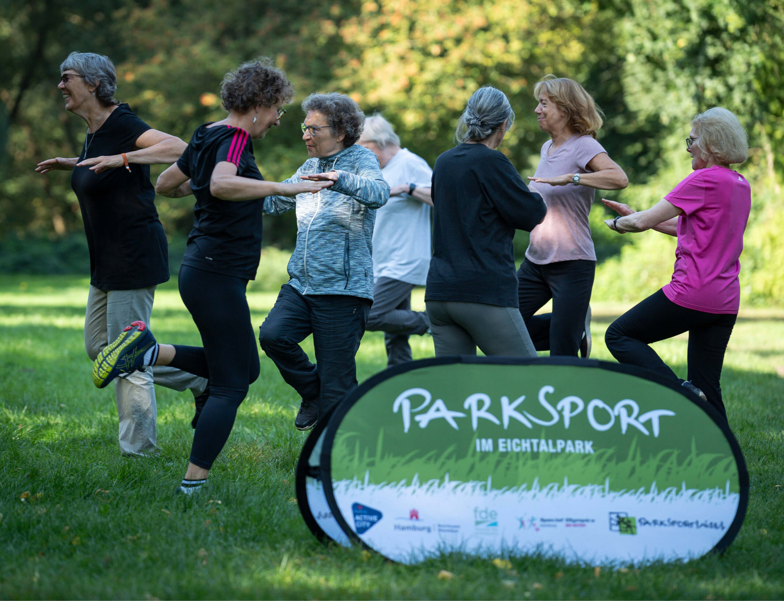 Gruppe älterer Frauen beim Sport im Hamburger Eichtalpark mit Beachbanner „Parksport im Eichtalpark“