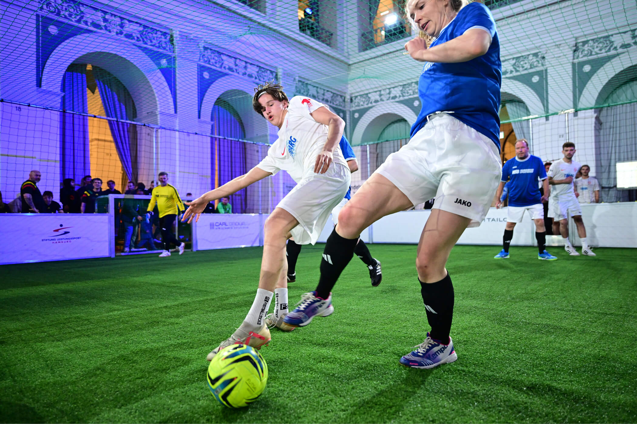 Frau vom Team HSB und Mann vom Team ETV im Zweikampf um den Ball beim Handelskammer Cup 2025 im Börsensaal Hamburg