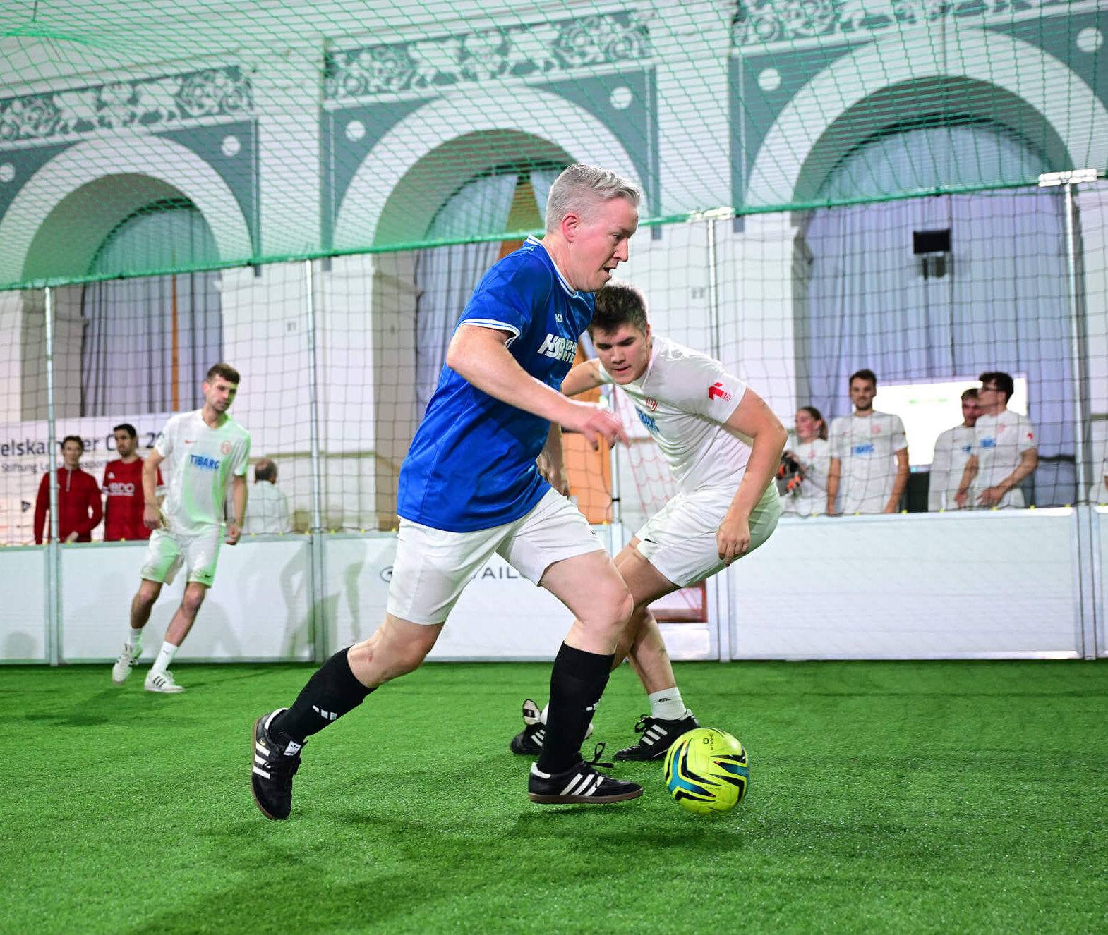 Drei Fußballspieler der Teams ETV und HSB beim Indoor-Spiel im Börsensaal der Handelskammer Hamburg mit Zuschauern
