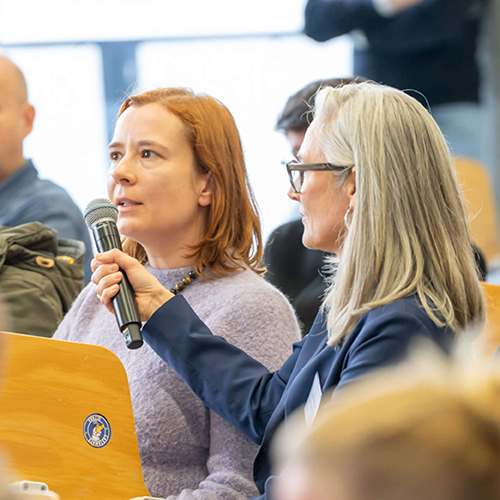 Zwei Frauen im Publikum einer Bürgerveranstaltung in Hamburg, eine hält der anderen ein Mikrofon für eine Wortmeldung zum Olympiakonzept.