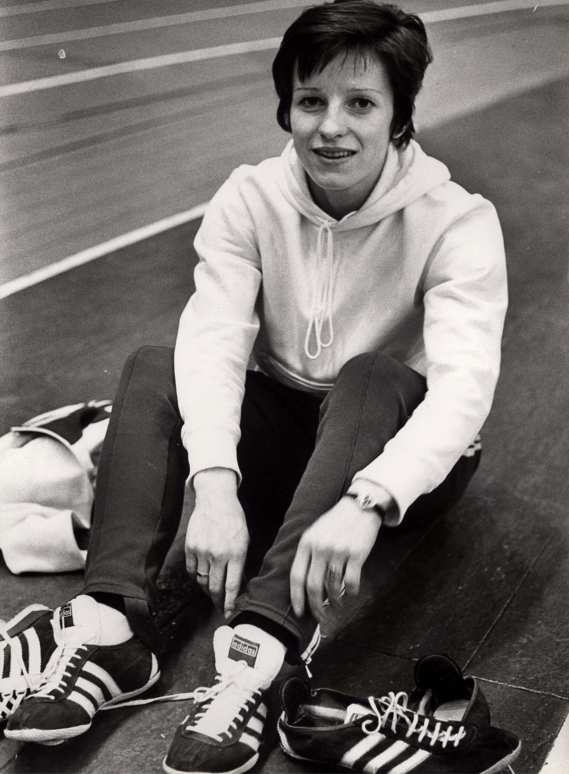 Schwarz-Weiß-Foto von Inge Bödding 1971 beim Anziehen ihres Laufschuhs neben der Tartanbahn im Training