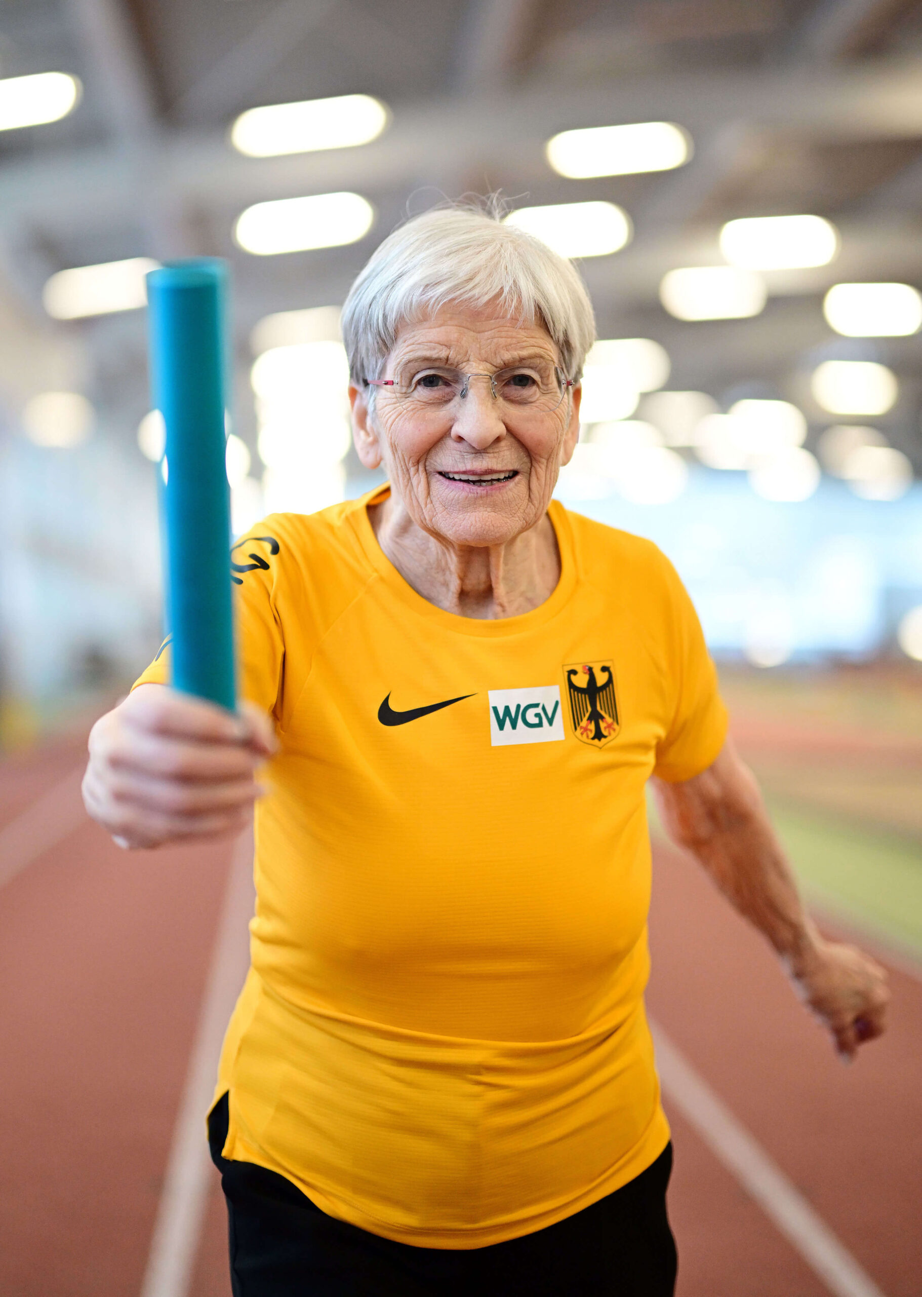Inge Bödding im Deutschlandtrikot hält lächelnd einen Staffelstab in der Hamburger Leichtathletikhalle