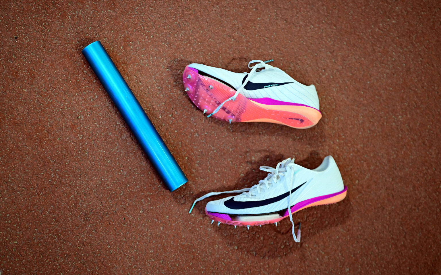 Türkise Laufschuhe und blauer Staffelstab auf einer Tartanbahn in der Leichtathletik