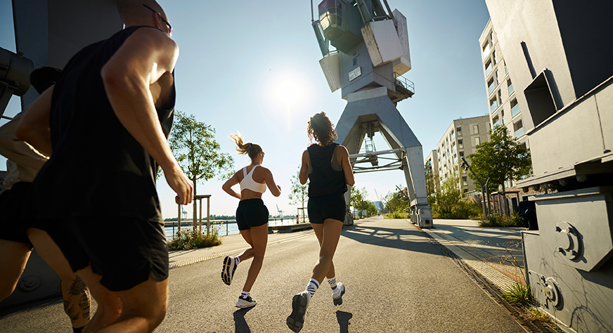 Vier Joggerinnen an der Promenade Kirchenpauerkai in der Hamburger HafenCity mit historischen Hafenkranen und Blick auf die Elbe
