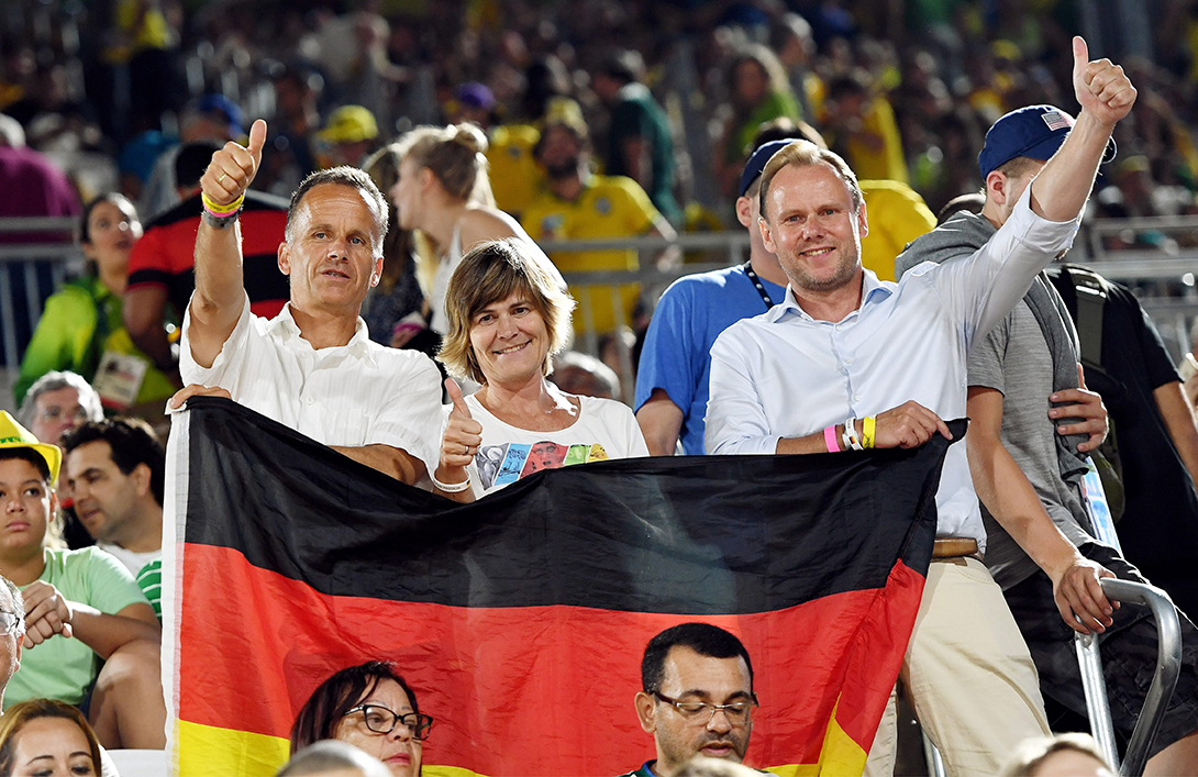 Christoph Holstein, Ingrid Unkelbach und Andy Grote jubeln mit Deutschlandflagge für Olympiasiegerin Laura Ludwig bei Rio 2016