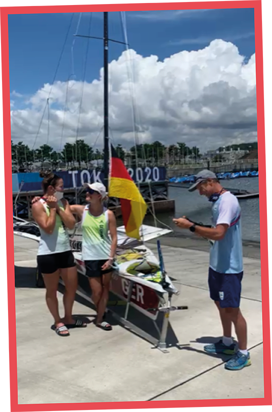 Seglerinnen Sanni Beucke und Tina Lutz lachen vor ihrem 49erFX Segelboot an Land bei Sonnenschein