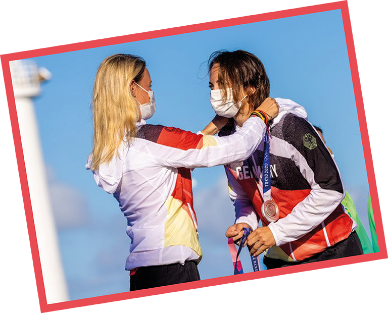 Seglerin Sanni Beucke erhält bei Olympia 2021 in Tokio die Silbermedaille von Teamkollegin Tina Lutz, beide mit Maske
