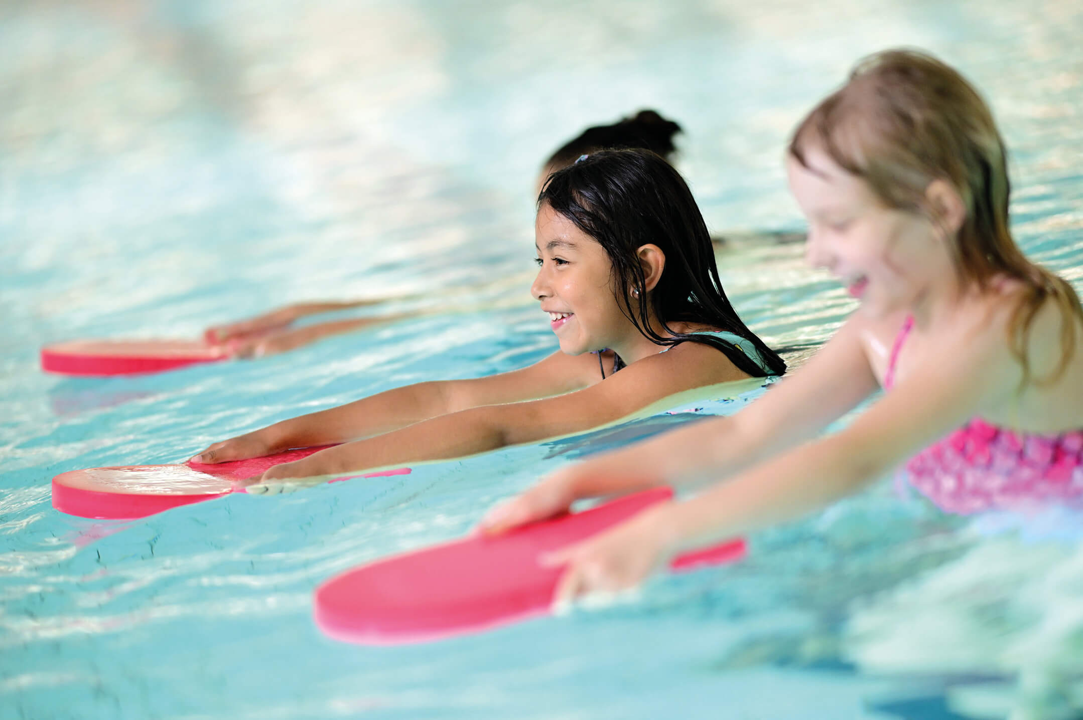Drei Mädchen mit rosa Schwimmbrettern im Schwimmbecken beim Schwimmenlernen in Hamburg